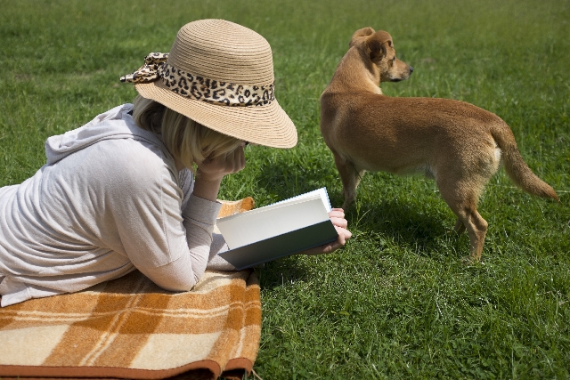 原っぱで読書する女性と犬