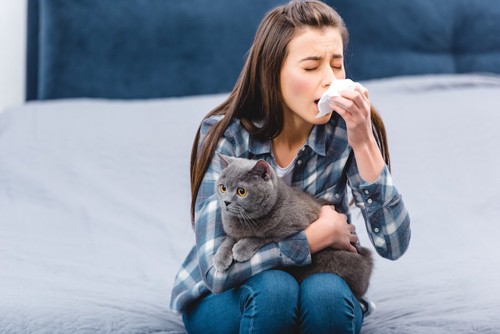 猫を抱いて鼻をかんでいるアレルギー持ちの女性