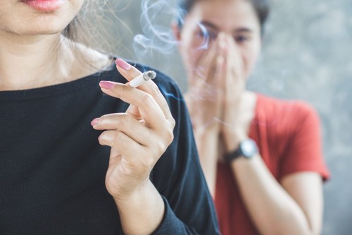 喫煙する女性の後ろで口元を押さえる女性