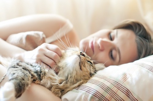 一緒の布団で眠る女性と猫
