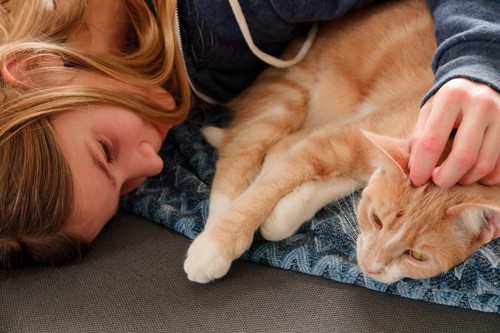 横になって猫を撫でる女性