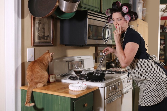 猫のそばでタバコを吸いながら料理をする女性