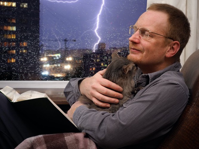 外の雷に怯える猫を優しく抱きしめる男性