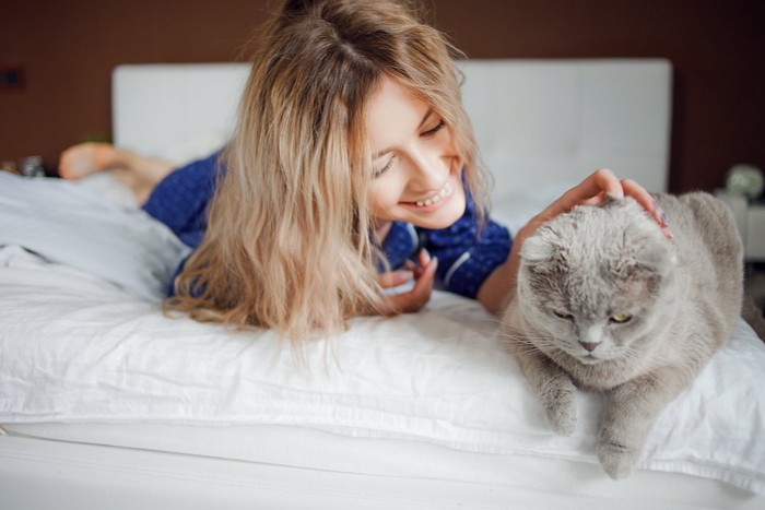 ベッドの上で猫を撫でる女性