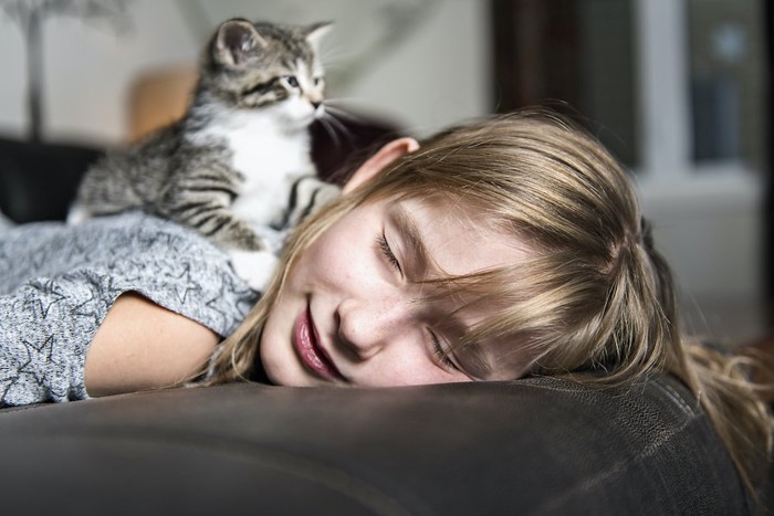うつ伏せで寝ている女性の背中に乗る猫