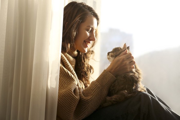 窓際で猫に笑顔を向ける女性