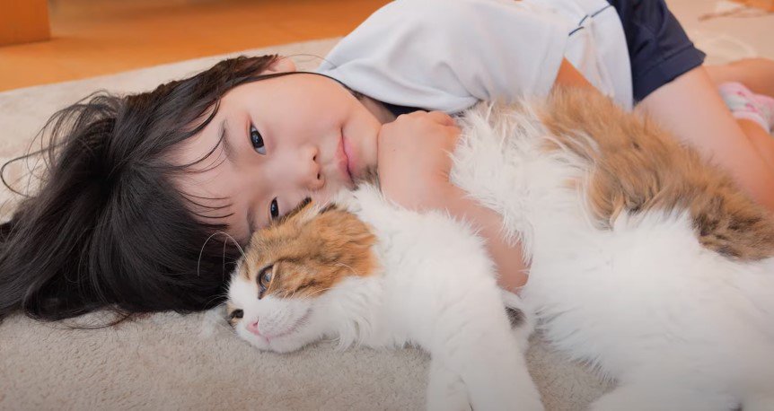 床の上で猫と寝転ぶ少女