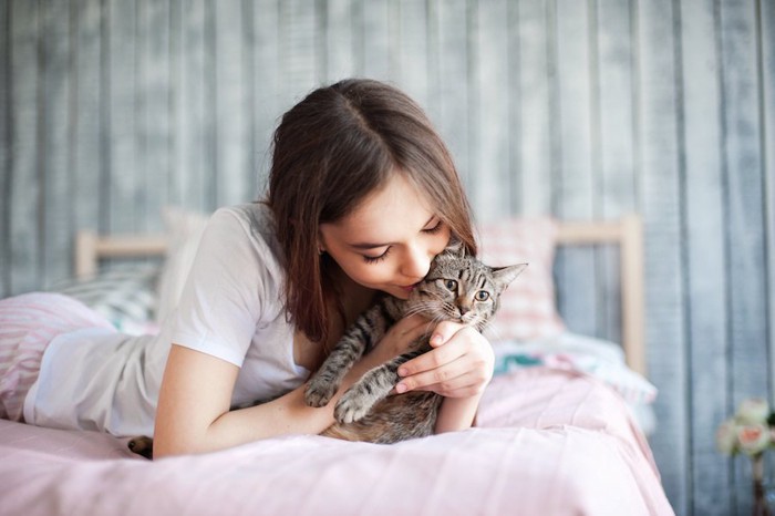 ベッドの上で猫を抱きしめる女性
