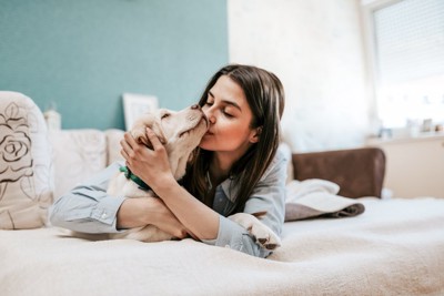 ベッドの上で犬をキスする女性
