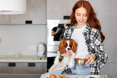 キッチンで料理する女性と抱っこされた犬