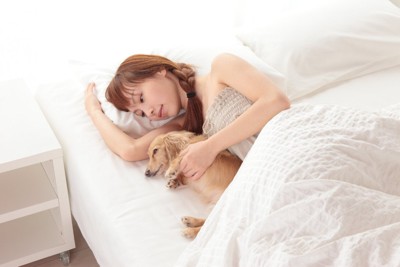 女性と一緒にベッドの上で横になる犬