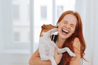 犬に顔を舐められて笑う女性