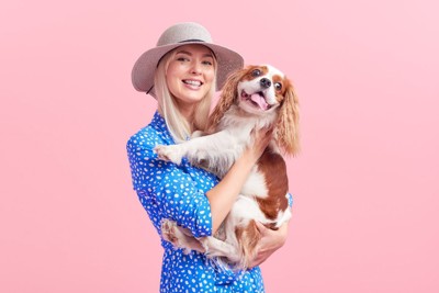 女性に抱っこされている犬とピンク背景