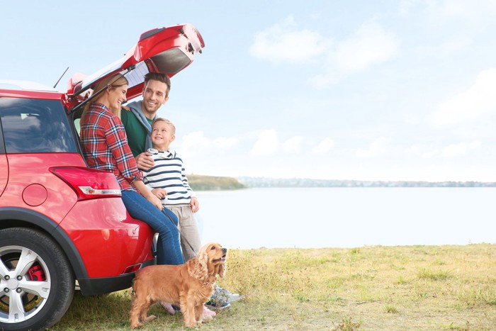 赤い車の近くに立つ家族と犬