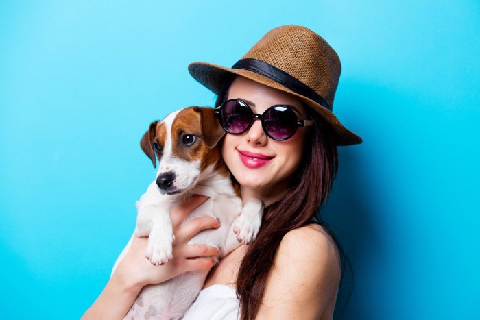 帽子とサングラスの女性に抱かれる犬
