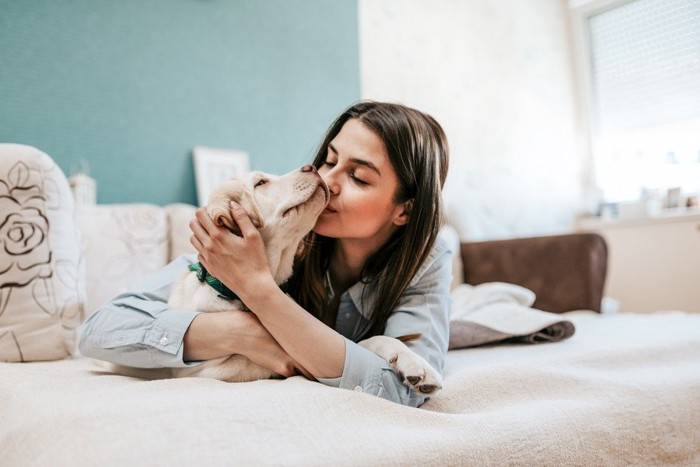 ベッドの上で犬にキスする女性