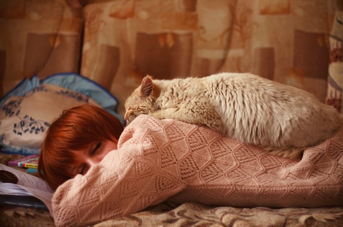 うつ伏せで眠る女性の背中で眠る猫