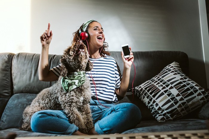 ソファーに座って歌う犬と音楽を聴く女性
