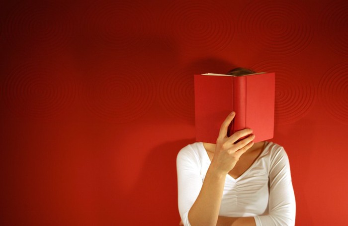 赤い本で顔を隠す女性