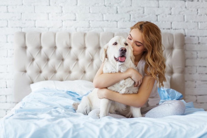 ベッドの上で犬を抱きしめる女性