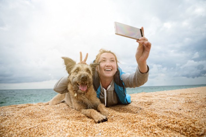 浜辺に寝転んで犬と自撮りする女性
